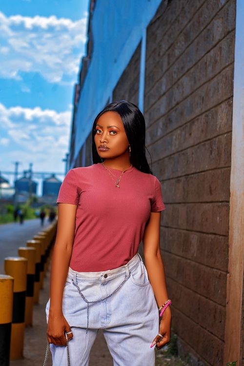 Free A fashionable young woman poses confidently against an urban backdrop with a clear blue sky. Stock Photo