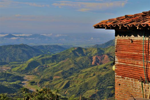 A rustic structure with clay tiles overlooking a lush mountainous landscape in daylight.