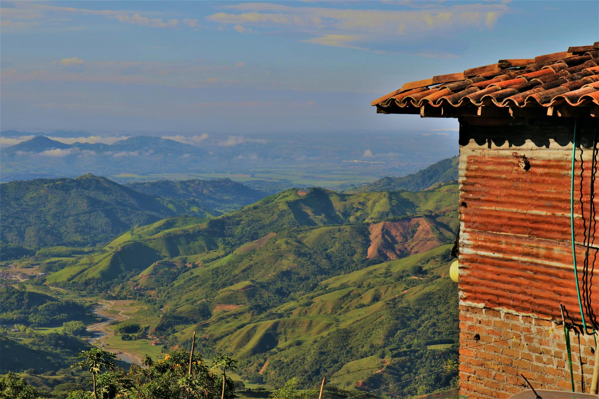 A rustic structure with clay tiles overlooking a lush mountainous landscape in daylight.