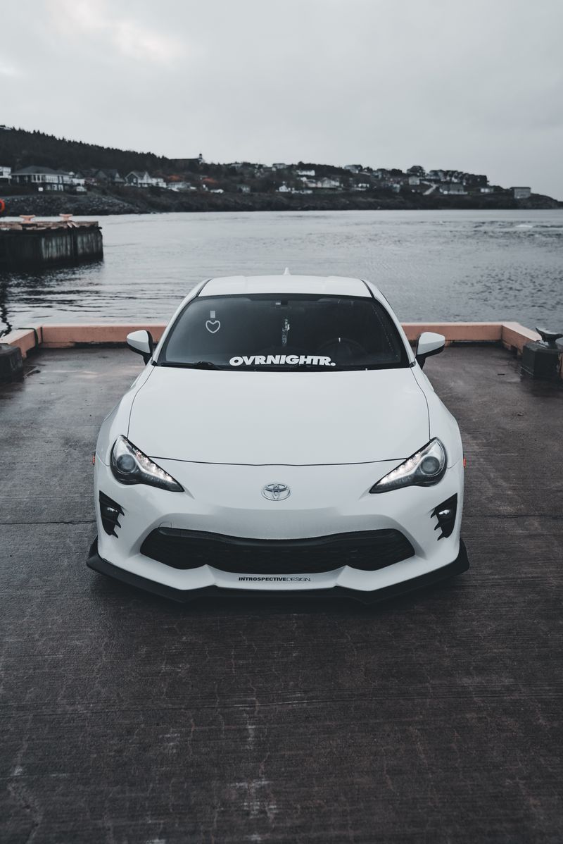 A sleek white sports car parked by a calm waterfront