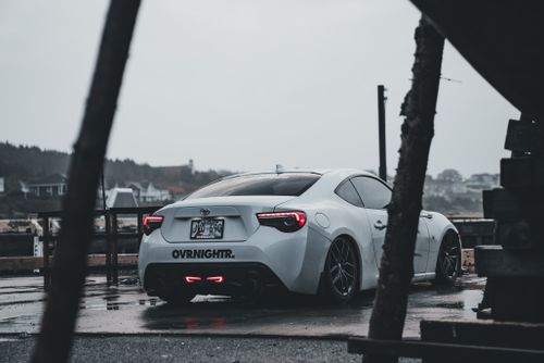 Free A stylish white sports car parked outdoors on a rainy day with a cityscape backdrop. Stock Photo