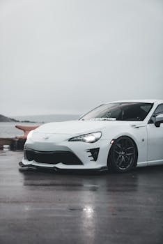 Capture of a white sports car on a rainy waterfront, showcasing its sleek design.