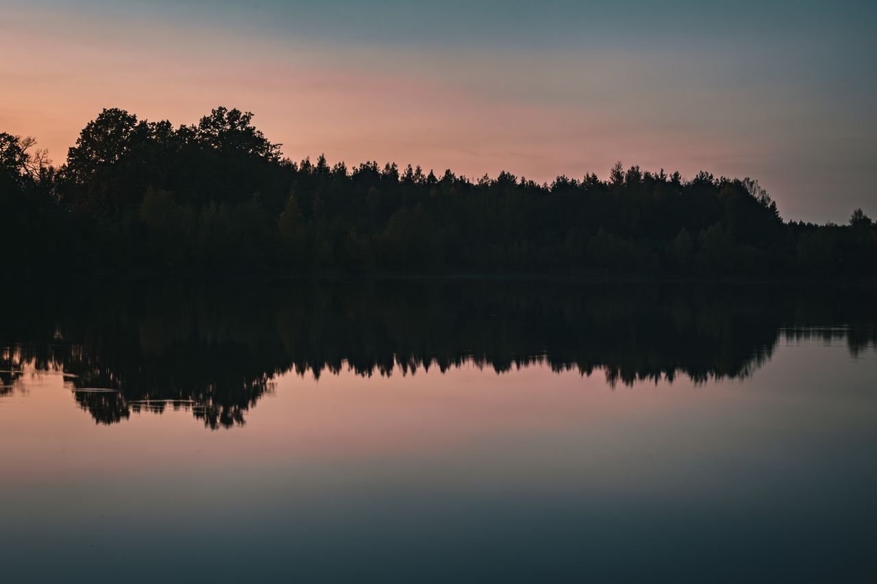 a tranquil sunset reflecting on a still lake framed by silhouetted tre