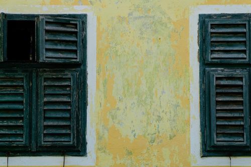Free Close-up of rustic wooden louvered shutters on a faded yellow wall, exuding a vintage charm. Stock Photo