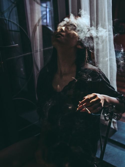 Free A captivating indoor portrait of a woman smoking, enveloped in dramatic shadows and smoke. Stock Photo