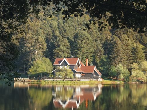 Free Picturesque house by a serene lake surrounded by lush forest. Stock Photo