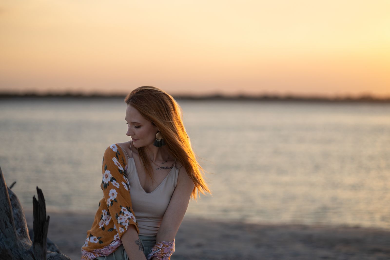Woman with long auburn hair in a floral kimono sitting by the water at sunset