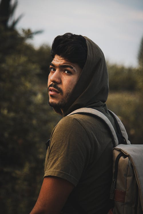 Selective Focus Photo of Man in Green Hooded T-shirt Carrying a Backpack