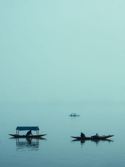 Free Calm lake scene featuring people in traditional Shikara boats enveloped in misty atmosphere. Stock Photo