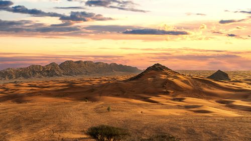 Free Vast desert landscape with sand dunes and mountains under a dramatic sunset sky. Stock Photo