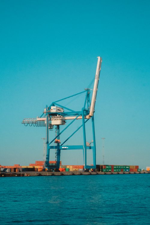 Free A large blue cargo crane at a shipping port with containers on a clear day. Stock Photo