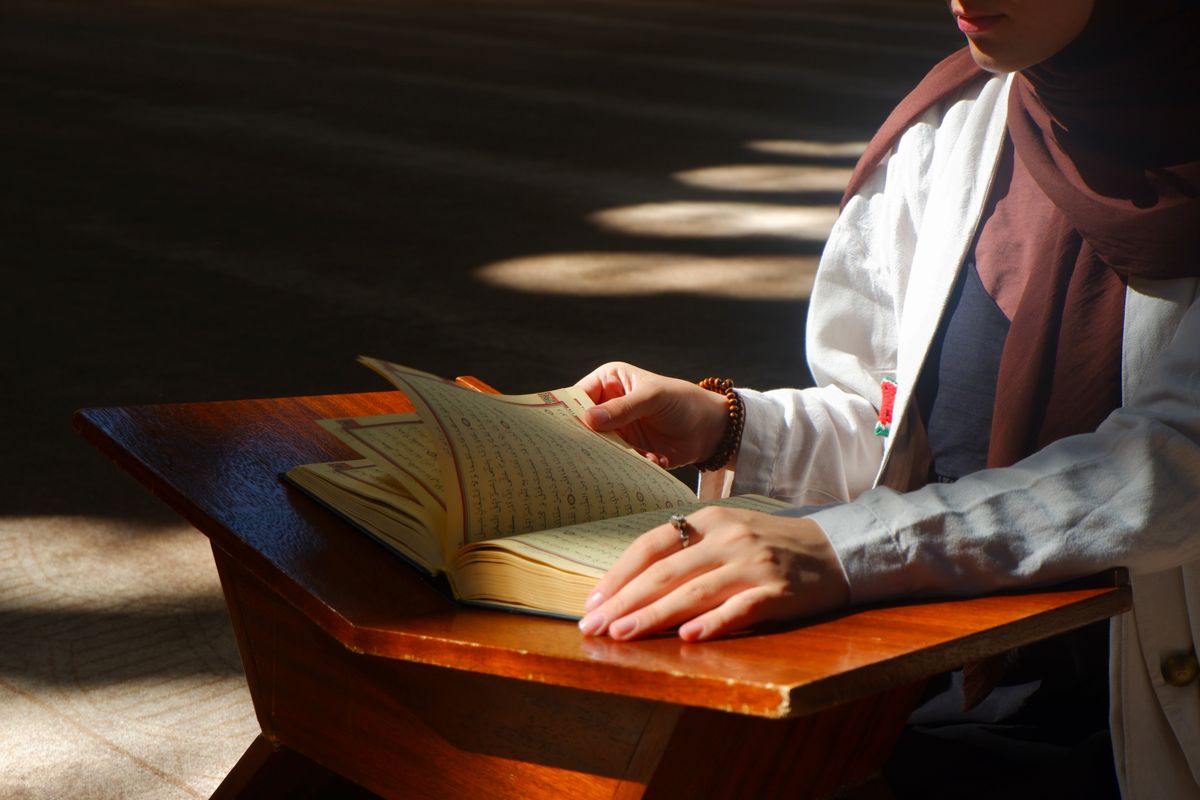 Woman reading Quran on wooden stand in sunlit mosque for Arabic and Noorani Qaida study