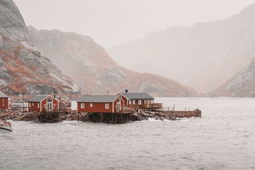 Free Red wooden houses on a fjord in Nusfjord, Norway, showcasing a serene and misty landscape. Stock Photo