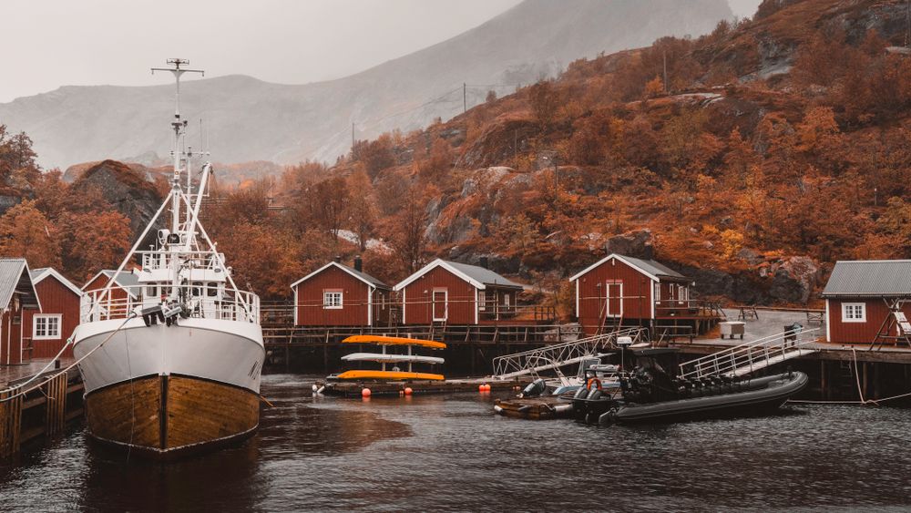Harbour boats and painted timber houses beneath a fjord ridge — photo by Raul Ling on Pexels
