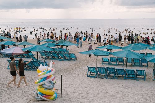 Free A vibrant beach scene with umbrellas and people enjoying the ocean under cloudy skies. Stock Photo