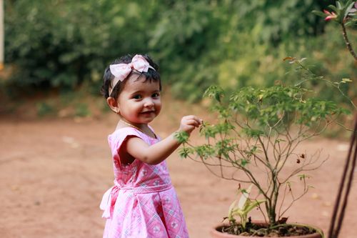 Free Cute toddler girl in pink dress playing with a potted plant outdoors. Stock Photo