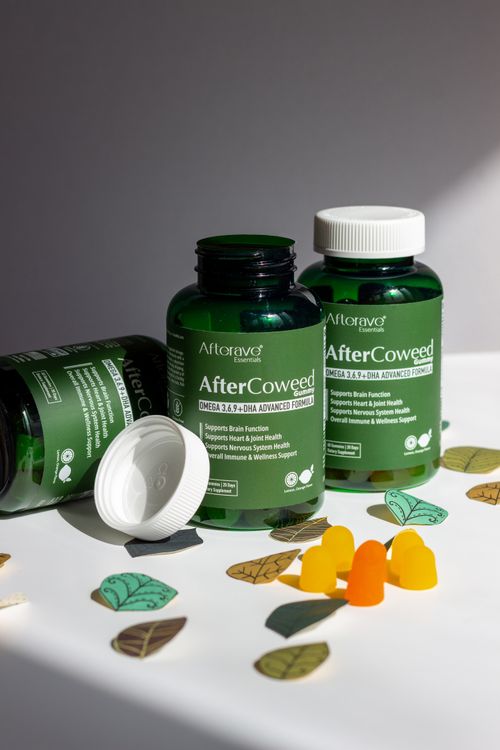 Free Green supplement bottles labeled 'AfterCoweed' with gummies and leaves on a white surface Stock Photo