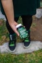 Person Holding Green Supplement Bottle Outdoors