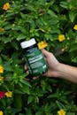 Hand Holding Supplement Bottle Among Flowers