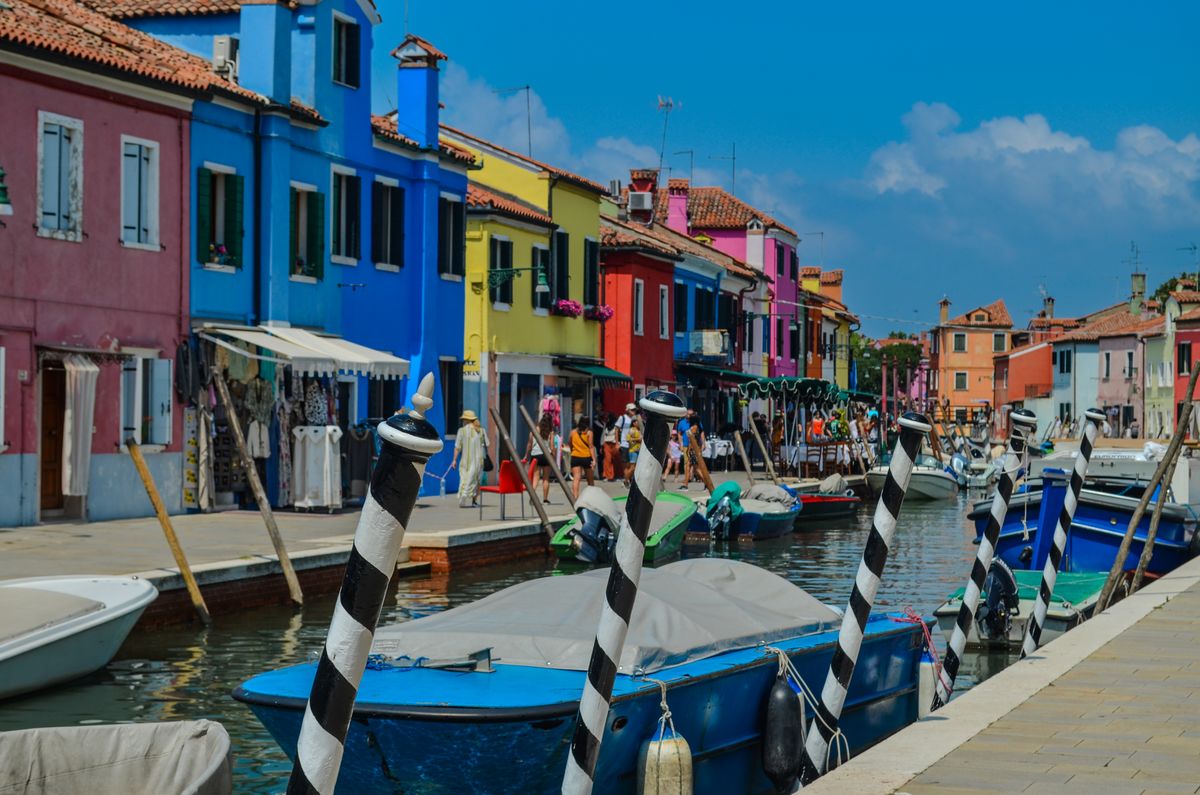 Vibrant, colorful houses lining Burano's canal with moored boats. Perfect Italian summer scene.