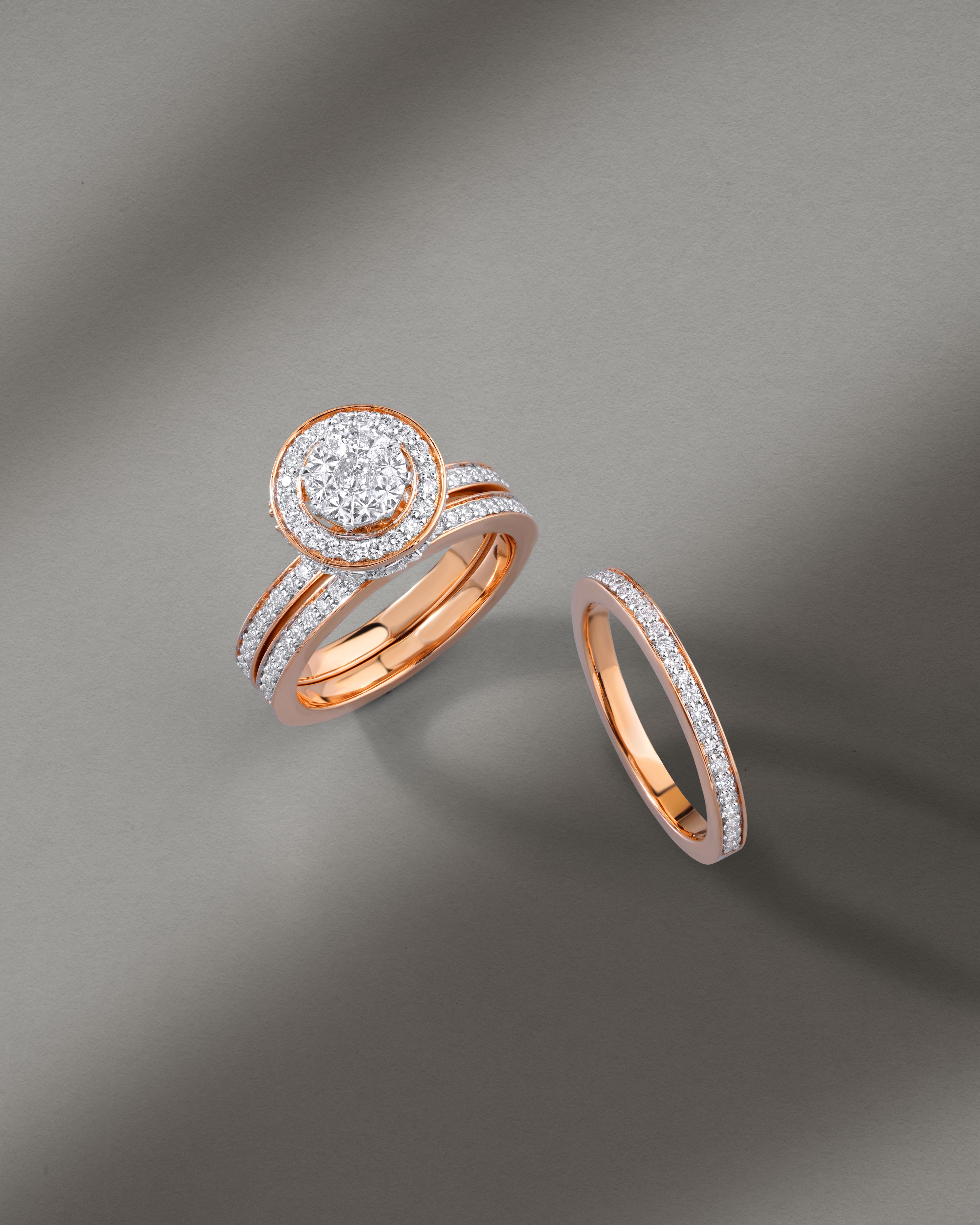 Exquisitos anéis de diamante com superfícies em ouro rosa exibidos em uma superfície cinza minimalista, destacando um design intricado.