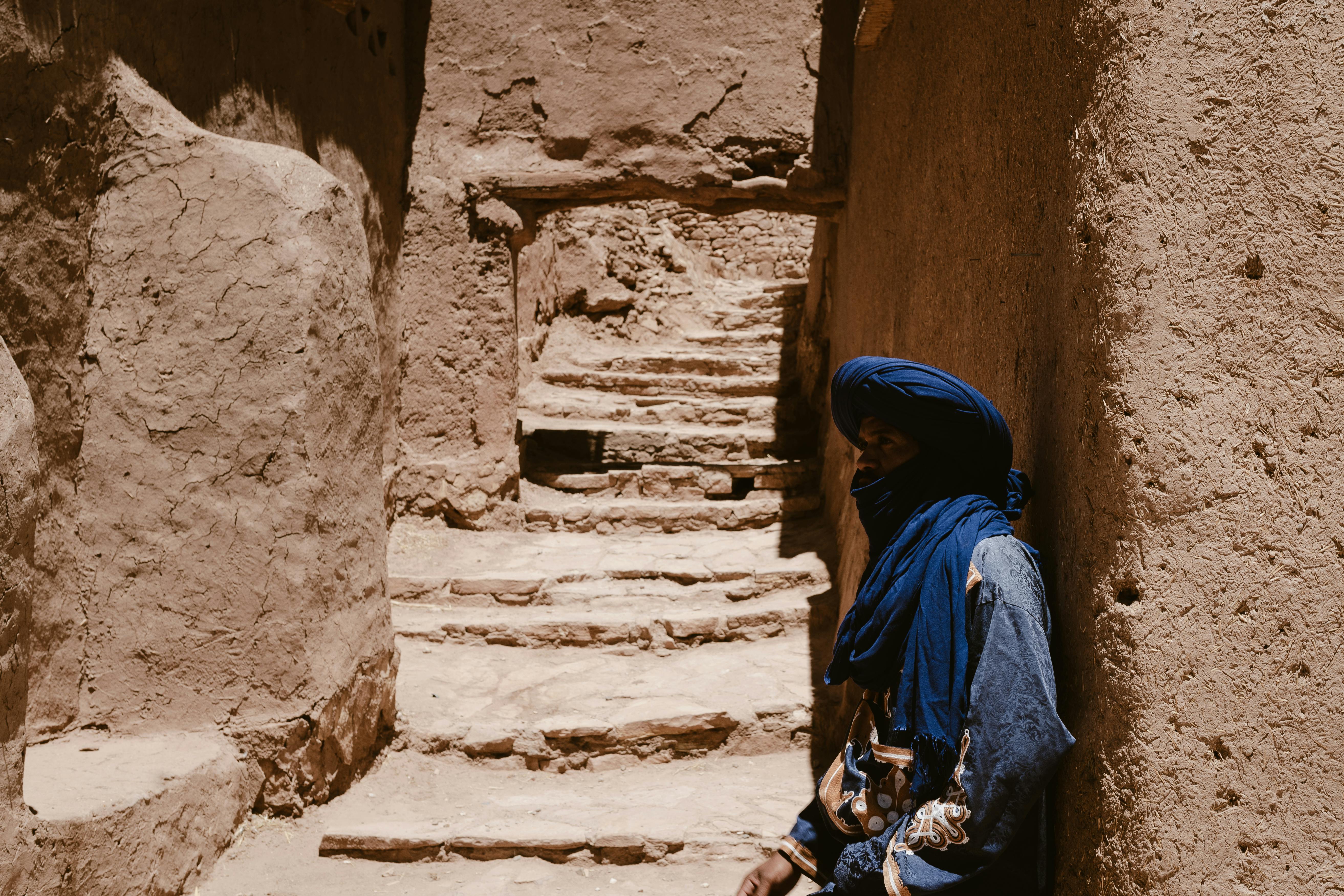 A Berber man in traditional attire stands in the ancient Ksar of Ait Benhaddou, Morocco.