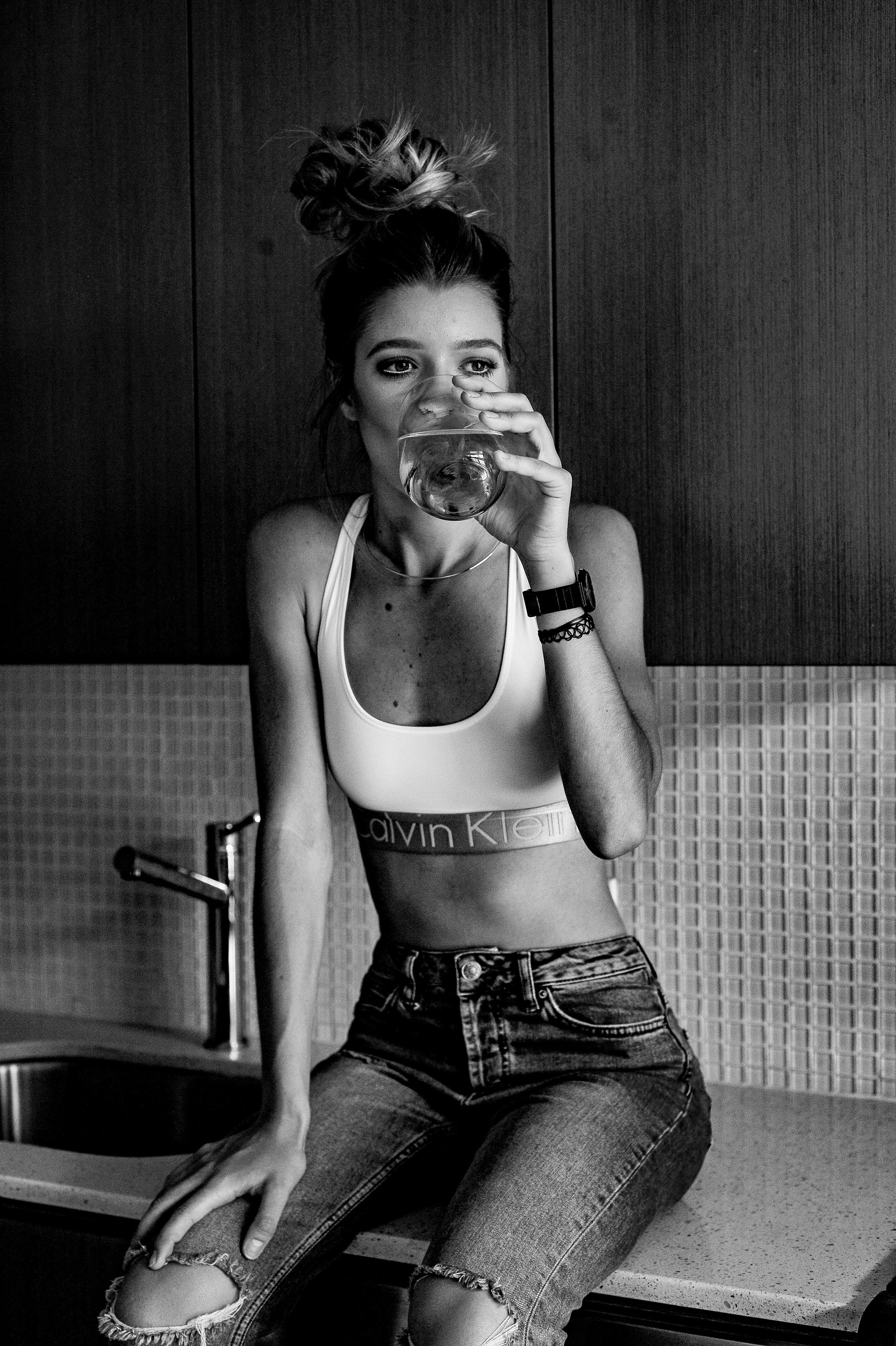 Black and white portrait of a woman in casual wear sipping a drink on a kitchen counter.