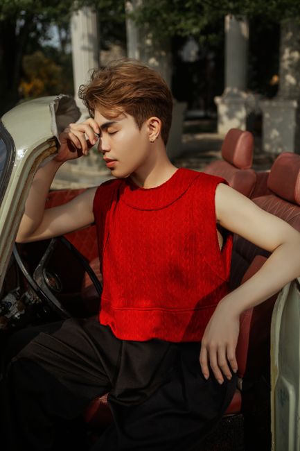 Youthful fashion portrait of a man in a vintage car wearing a vibrant red top.
