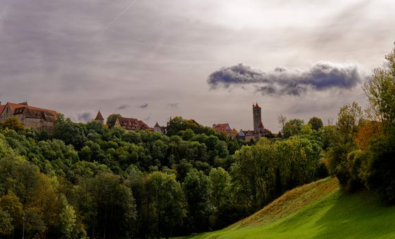 Scenic view of Rothenburg ob der Tauber's medieval skyline framed by lush autumn trees.