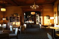 Elegant rustic restaurant interior featuring log walls, chandeliers, and classic wooden furniture.