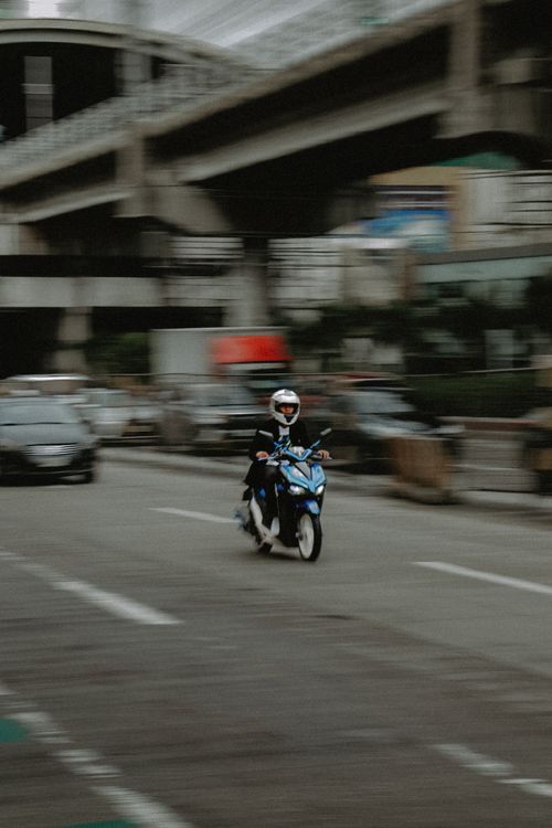 Free Dynamic panning shot of a blue motorcycle speeding through a bustling street in Quezon City, Manila. Stock Photo