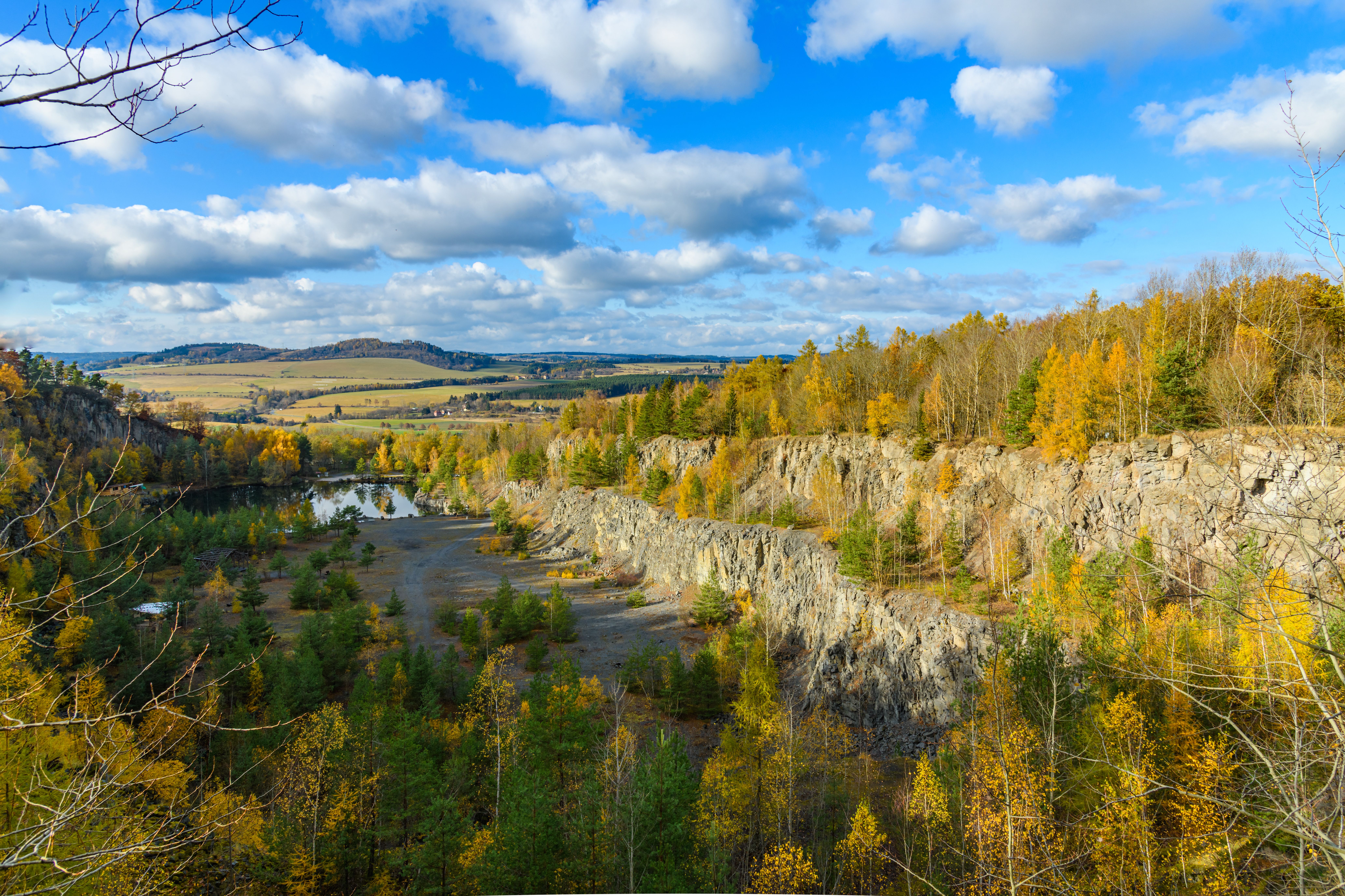 Colorful autumn view of a flooded quarry in Czechia with a scenic forest and rocky terrain.