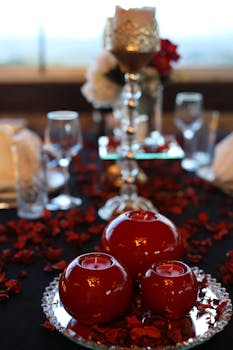 Romantic dining setup with red candles and petals for a cozy ambiance.