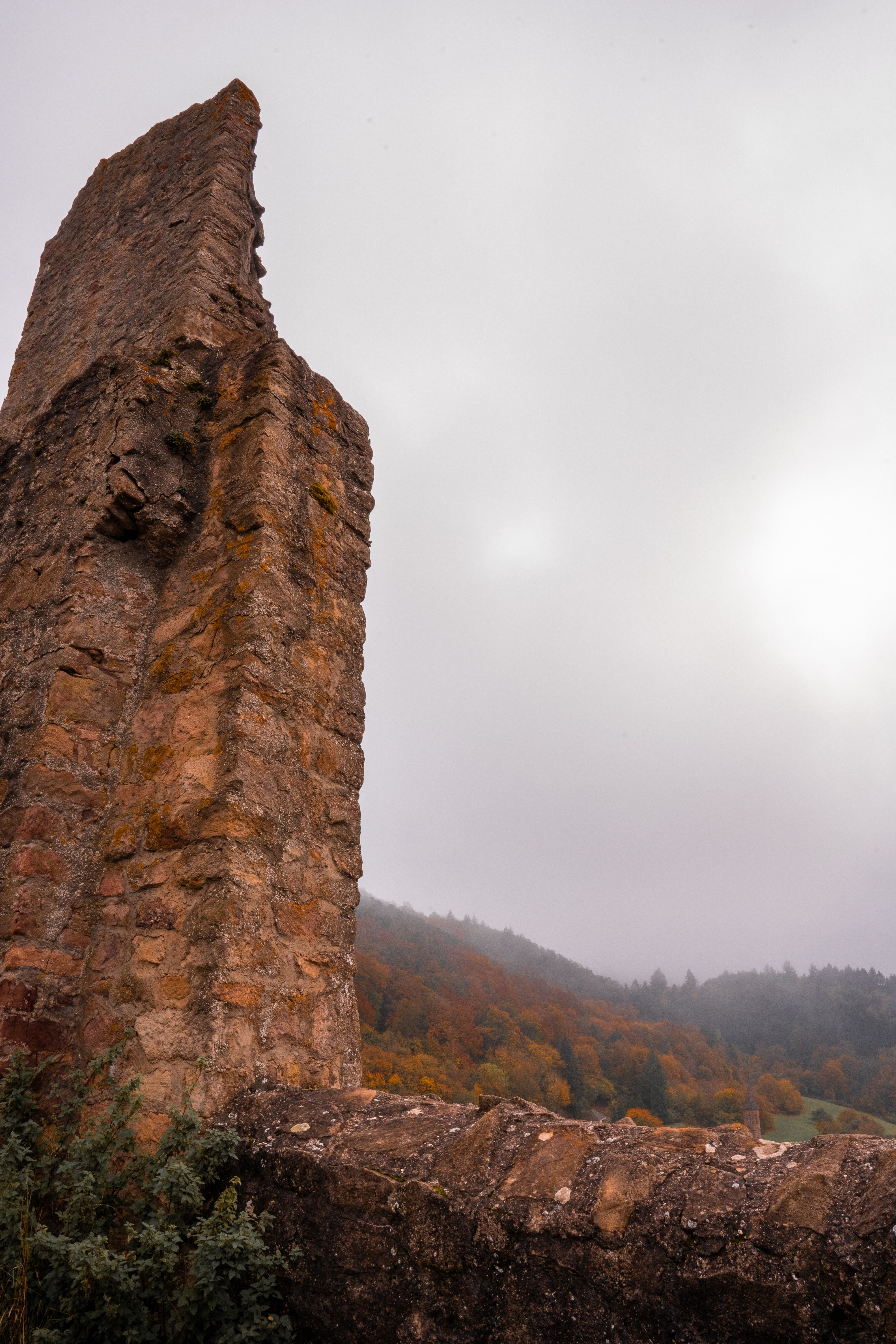 Tall ancient stone ruin against a cloudy sky, with a misty autumn forest in the background.