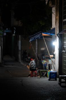 Nighttime urban scene of street vendors in an alley, captured in a moody, low-light setting.