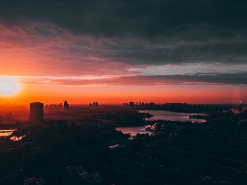 Free Dramatic sunset casts vibrant hues over city skyline with silhouetted buildings and river. Stock Photo