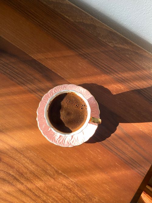 Free A charming coffee cup casting a shadow on a wooden table under warm sunlight. Stock Photo