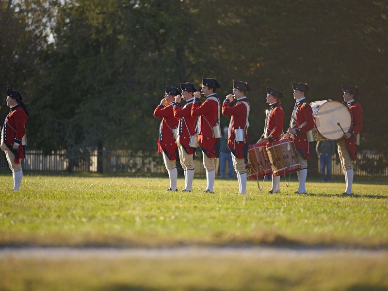 Colonial-era military band reenacting history in open field - colonial history sites