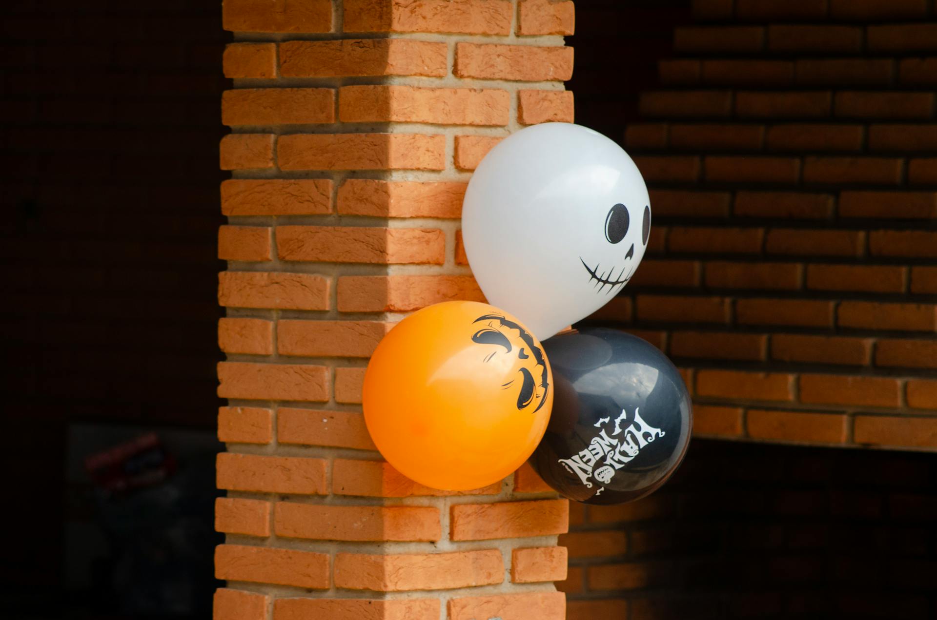 Halloween-themed balloons with spooky designs on a brick wall.