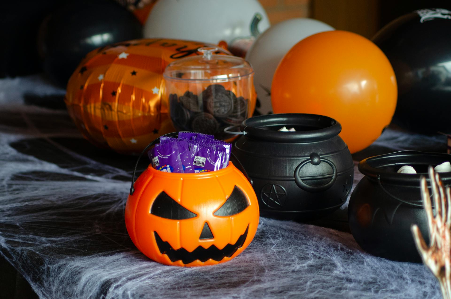 Halloween themed candy display with a pumpkin bucket and cauldrons on a decorated table.