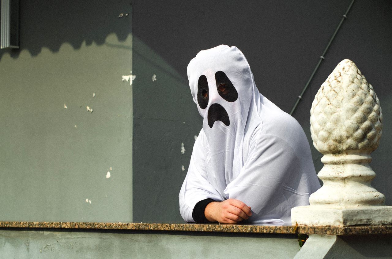 person in a ghost costume standing on a balcony with a spooky expressi