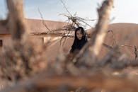 一位身着长袍的女子，静立于沙漠的浮木旁，在宁静的风景中捕捉到孤独与美丽