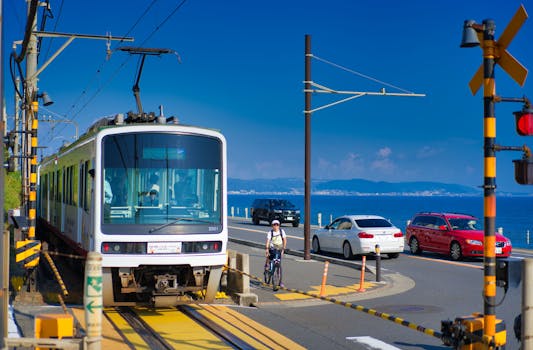 A vibrant scene of a tram crossing by the coast in Kamakura, Japan, with cyclists and cars nearby.