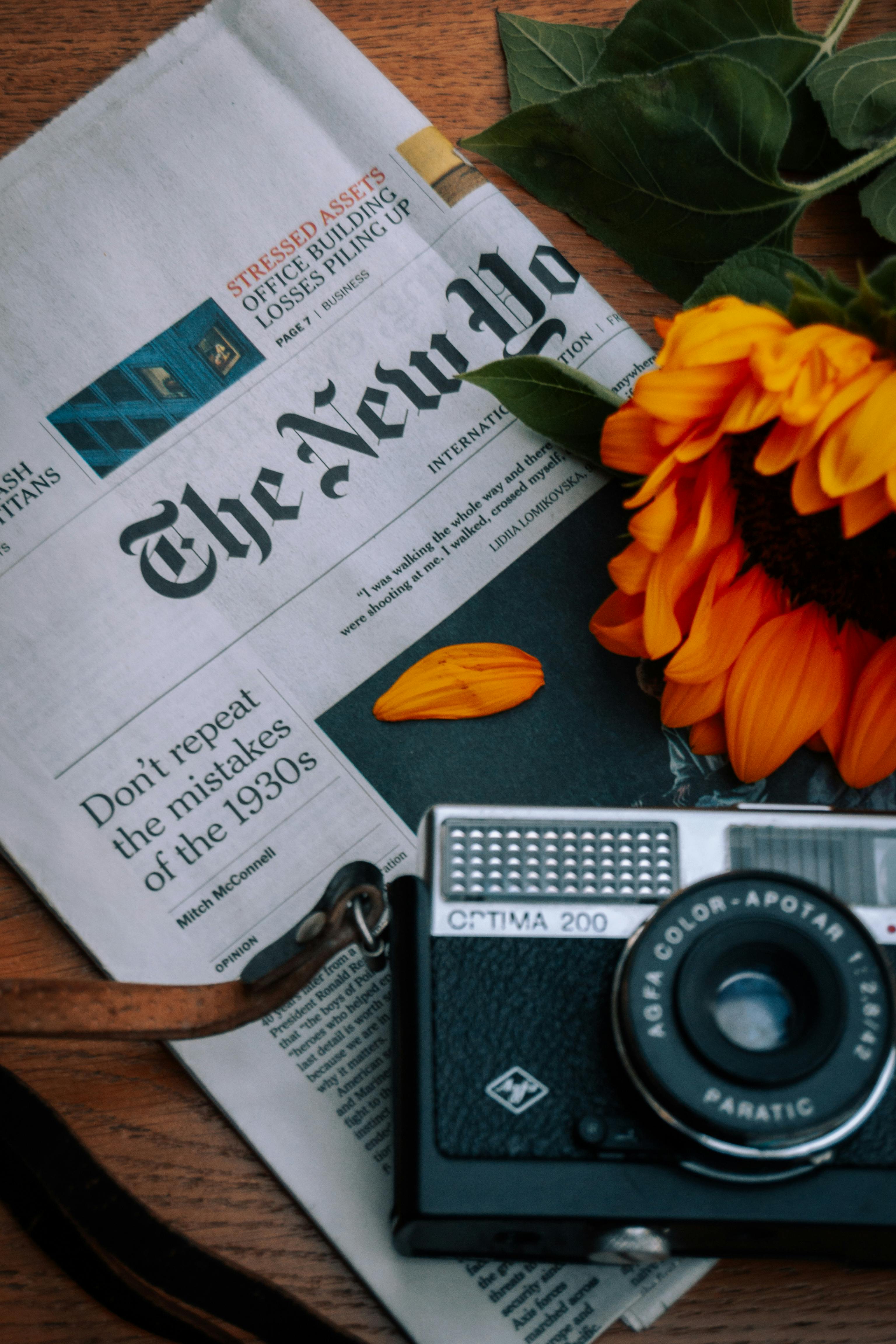 A classic camera and sunflower on a New York Times newspaper evoke nostalgia and artistry.