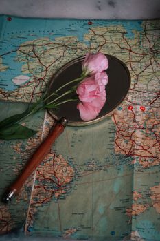 Pink flowers reflect in a handheld mirror on a vintage map. Elegant and nostalgic composition.
