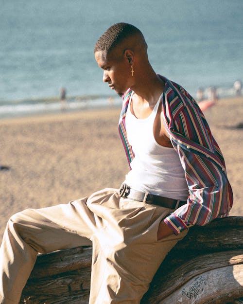 A Man Sitting On A Tree Trunk By The Beach