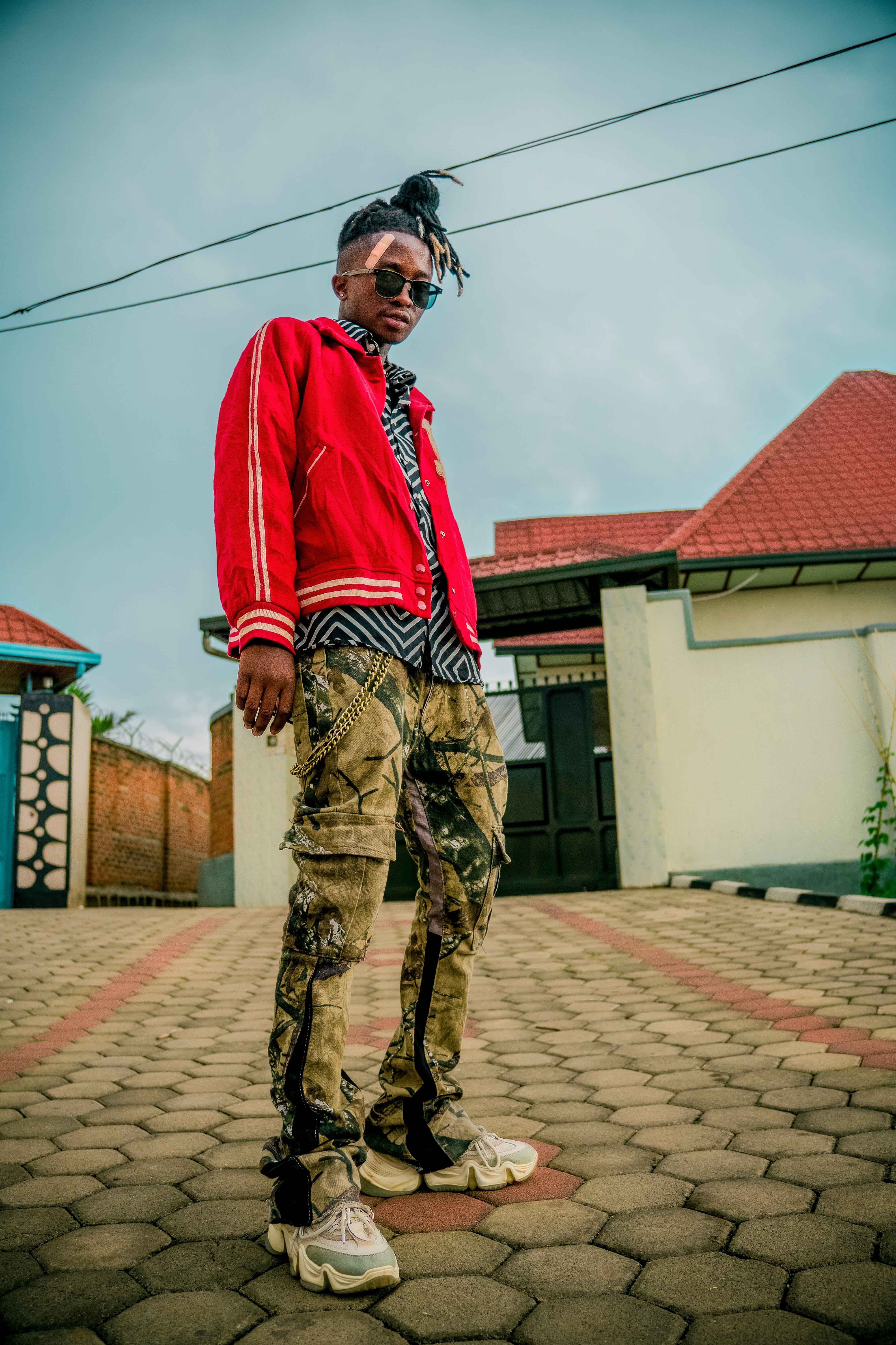Man in trendy attire standing on a paved street in an urban area.
