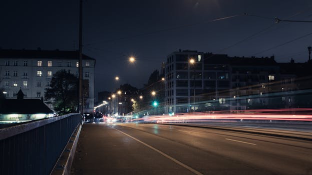 Urban night scene in Munich, Germany, showcasing street lights and vehicle light trails on a quiet road.