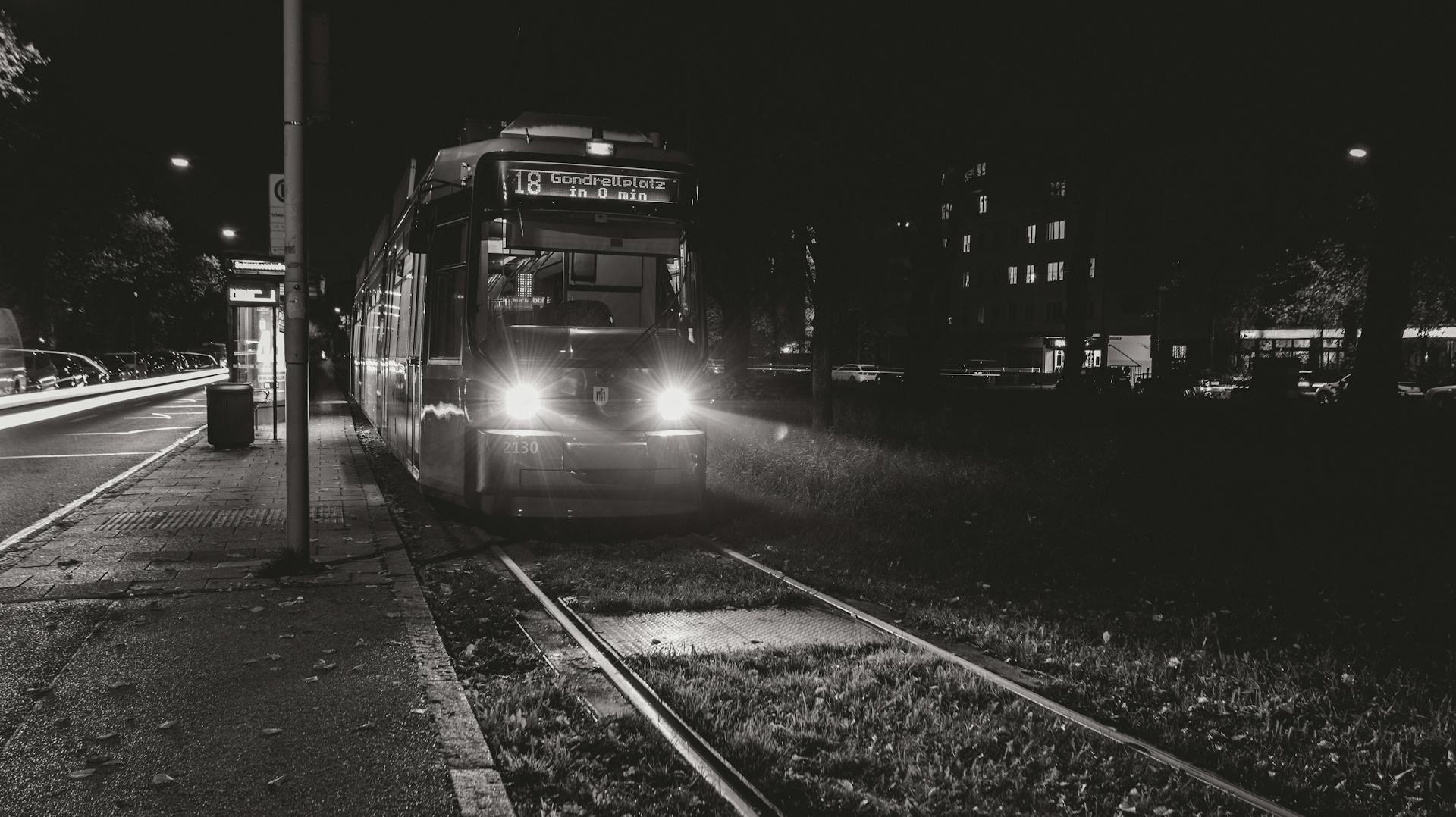 A black and white photo of a tram in München at night with headlights on.