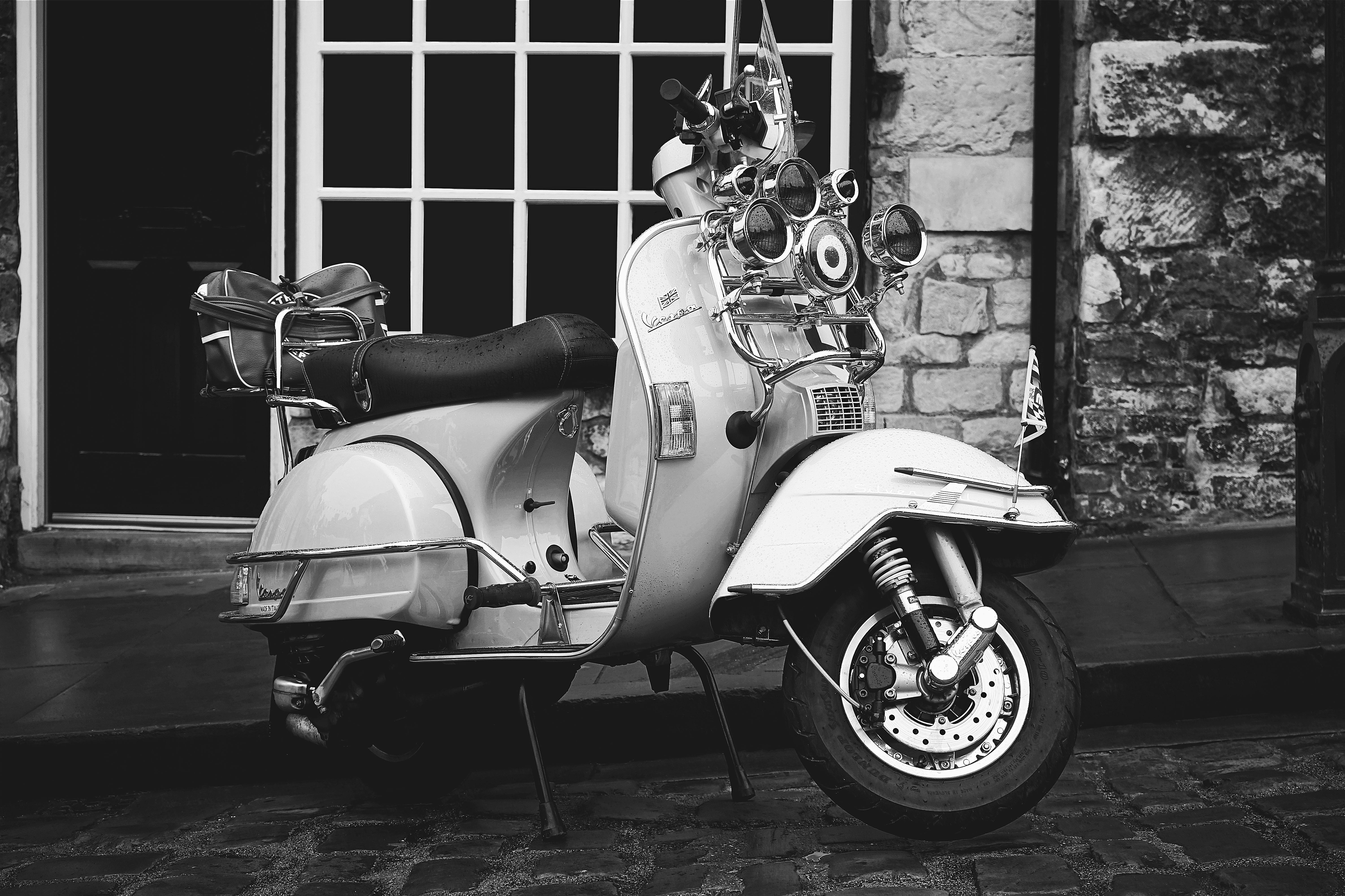 A nostalgic black and white photo of a vintage scooter parked outdoors.